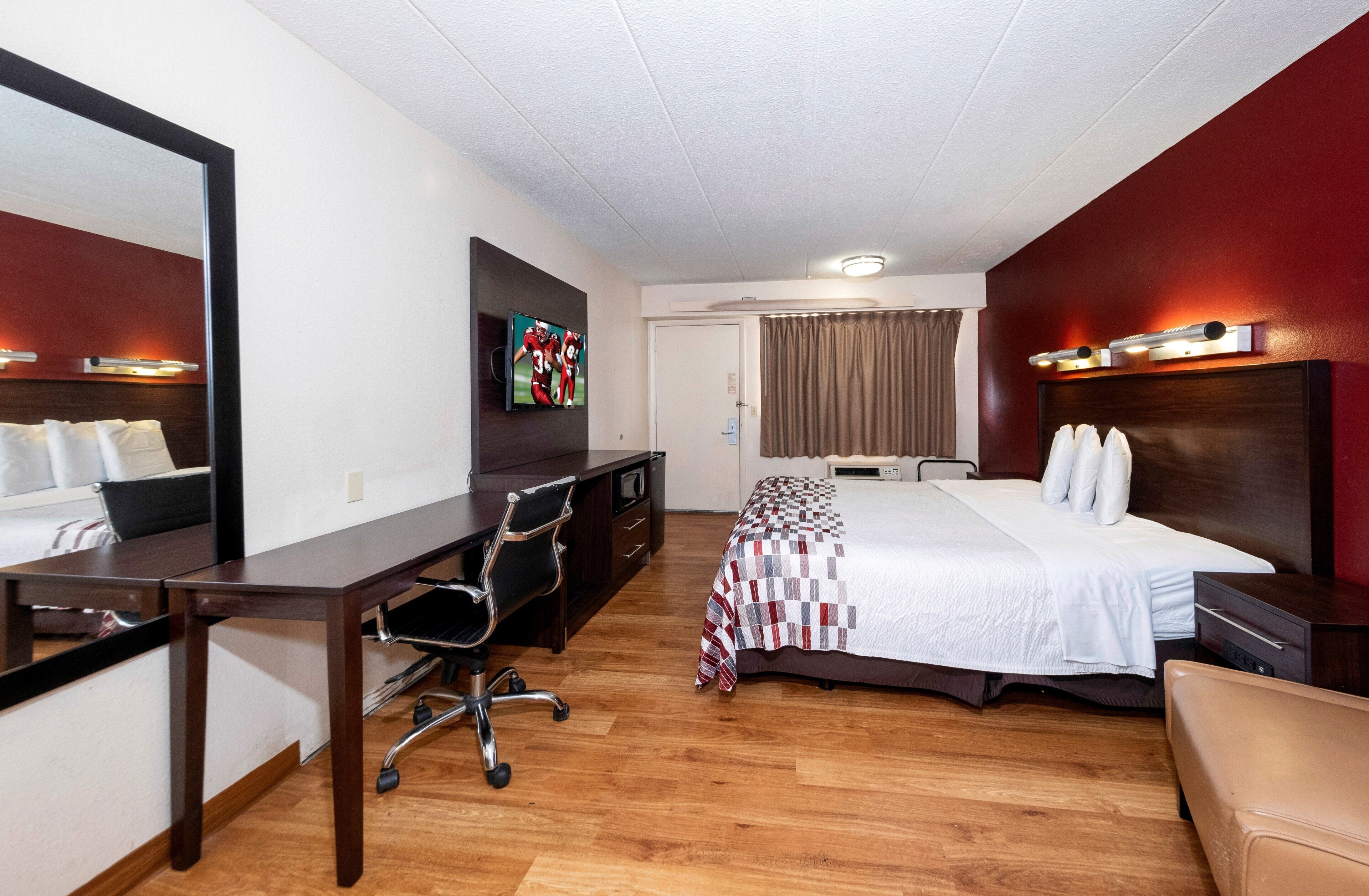 Una habitación de hotel con cama, escritorio, silla y televisor en la pared.