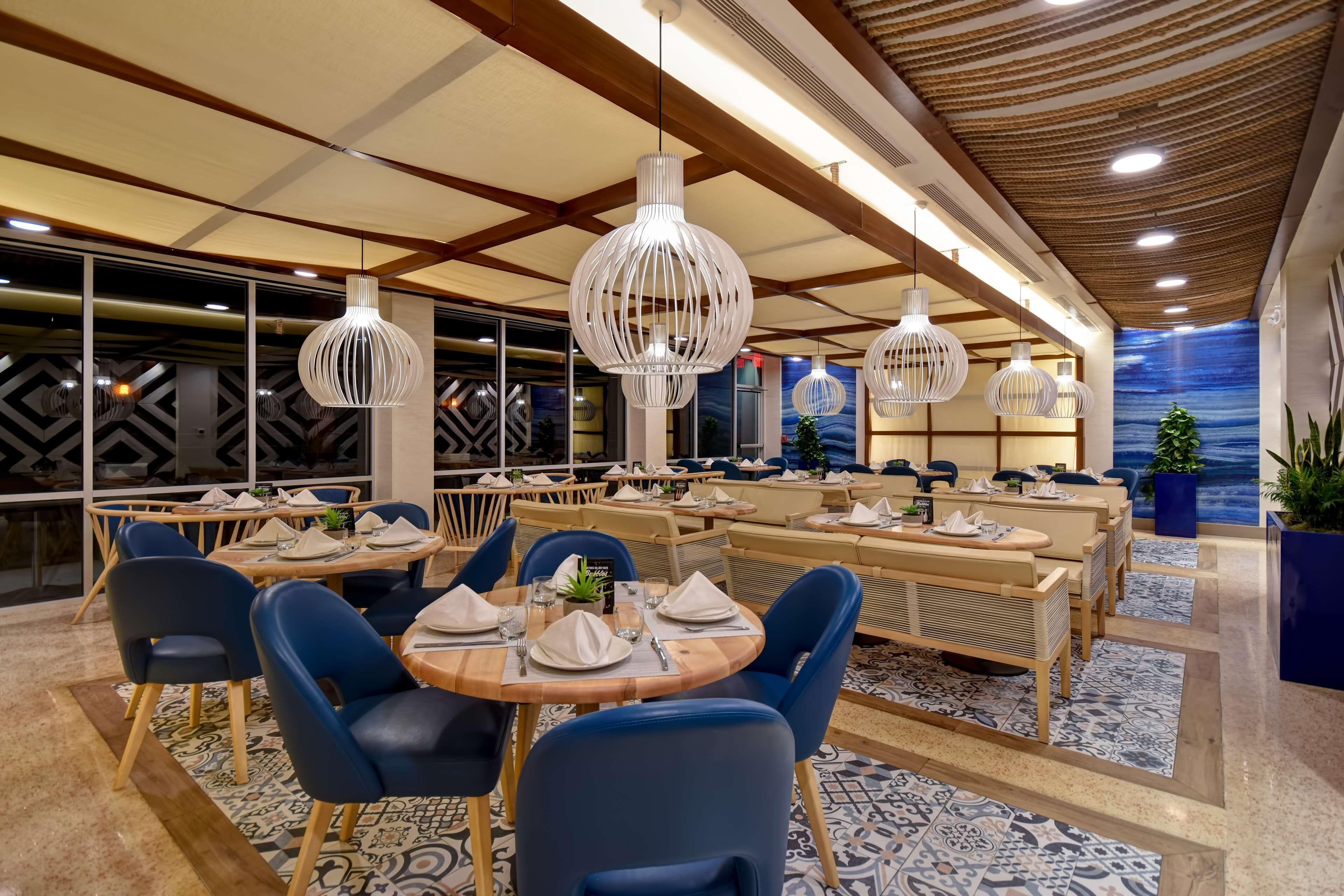 Un restaurant moderne avec des tables rondes, des chaises bleues et des luminaires suspendus blancs.