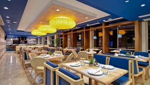A modern restaurant with wooden tables and blue cushioned booths, yellow pendant lights, and a polished floor.