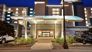 A modern hotel entrance with a glass facade, a sign reading "DOUBLETREE by Hilton," and a covered walkway leading to the entrance.