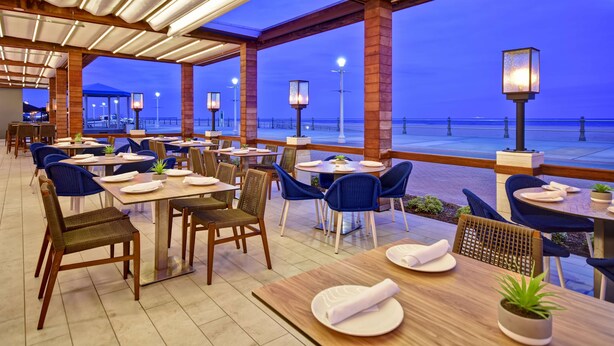 A restaurant with tables and chairs, a view of the beach, and a covered outdoor area with lights.