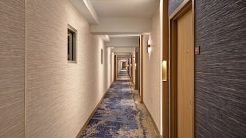 Un pasillo de hotel con alfombra estampada, puertas de madera y pared de color claro.