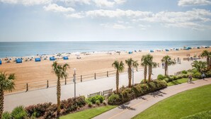A beach with a paved walkway, palm trees, and beach umbrellas.