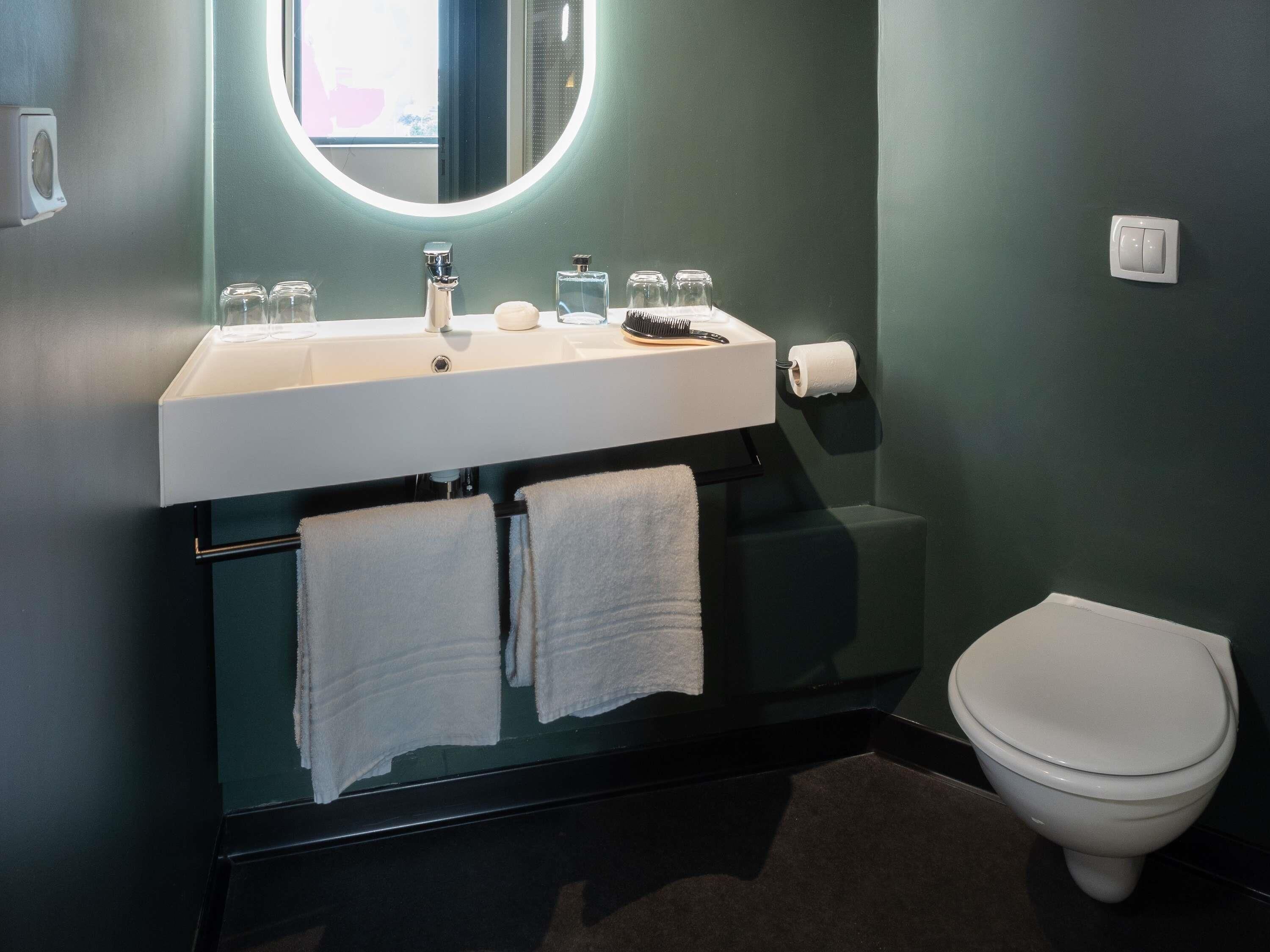 A modern bathroom with a white sink, mirror, and toilet. There are two towels hanging on a rack.