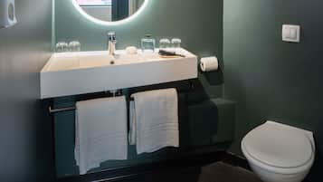 A modern bathroom with a white sink, mirror, and toilet. There are two towels hanging on a rack.