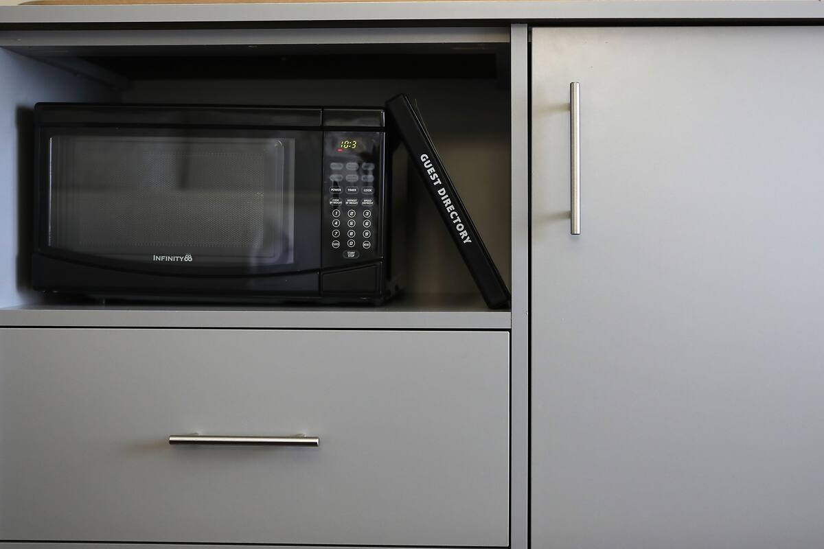 A microwave in a kitchen cabinet with a guest directory.