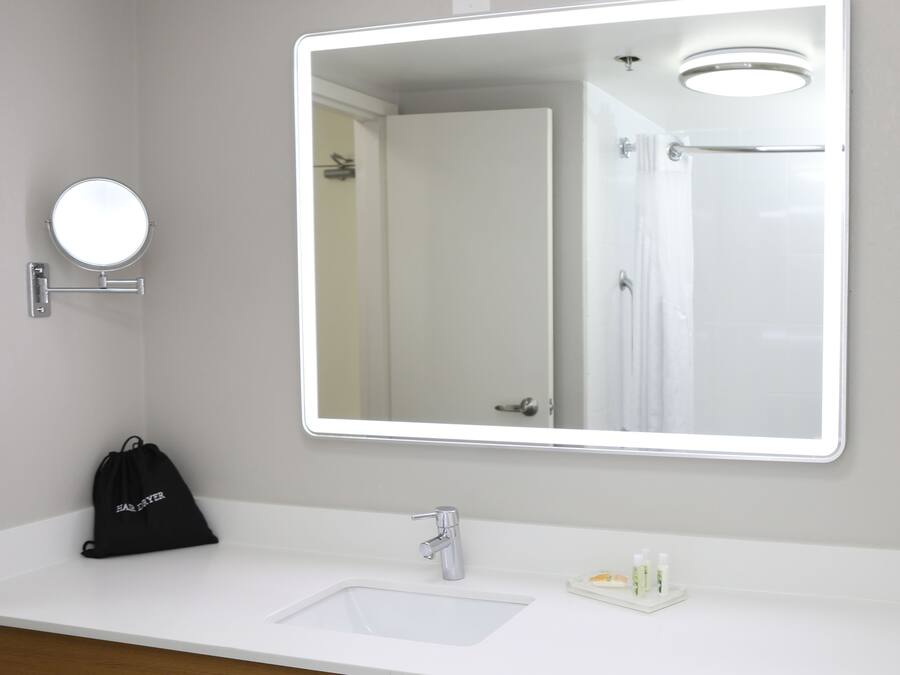 A bathroom with a large mirror, a sink, a black bag, and a small bottle on the counter.
