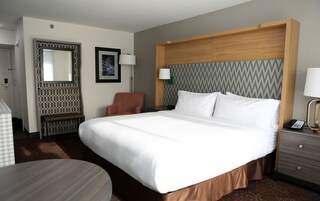 Habitación de hotel con una cama grande, una silla, un escritorio, un espejo y una pared con diseño decorativo.
