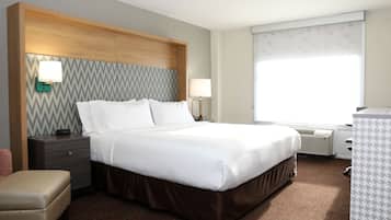 A hotel room with a large bed, a wooden headboard, two bedside tables with lamps, a bench, and a large window with a view.