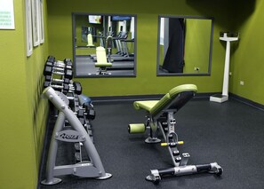 A gym with exercise equipment, mirrors, and a green wall.