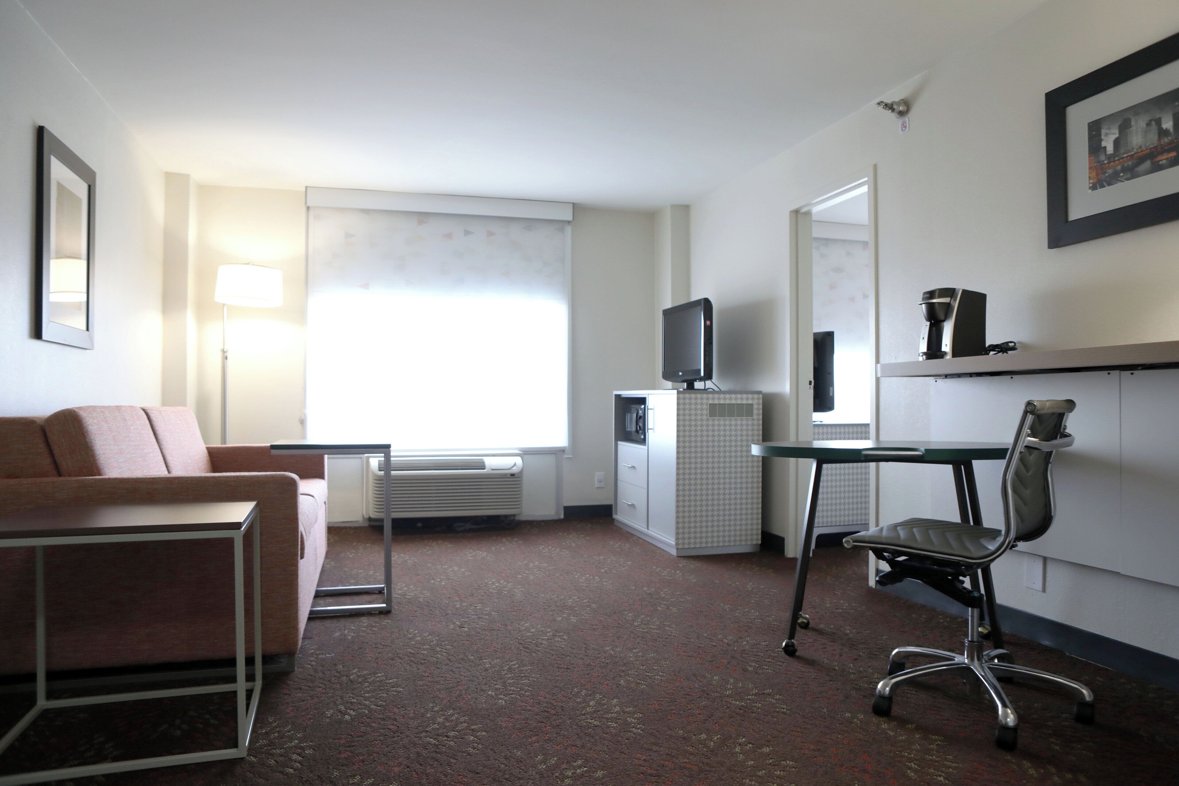 A hotel room with a sofa, a desk, a chair, a television, and a coffee machine.