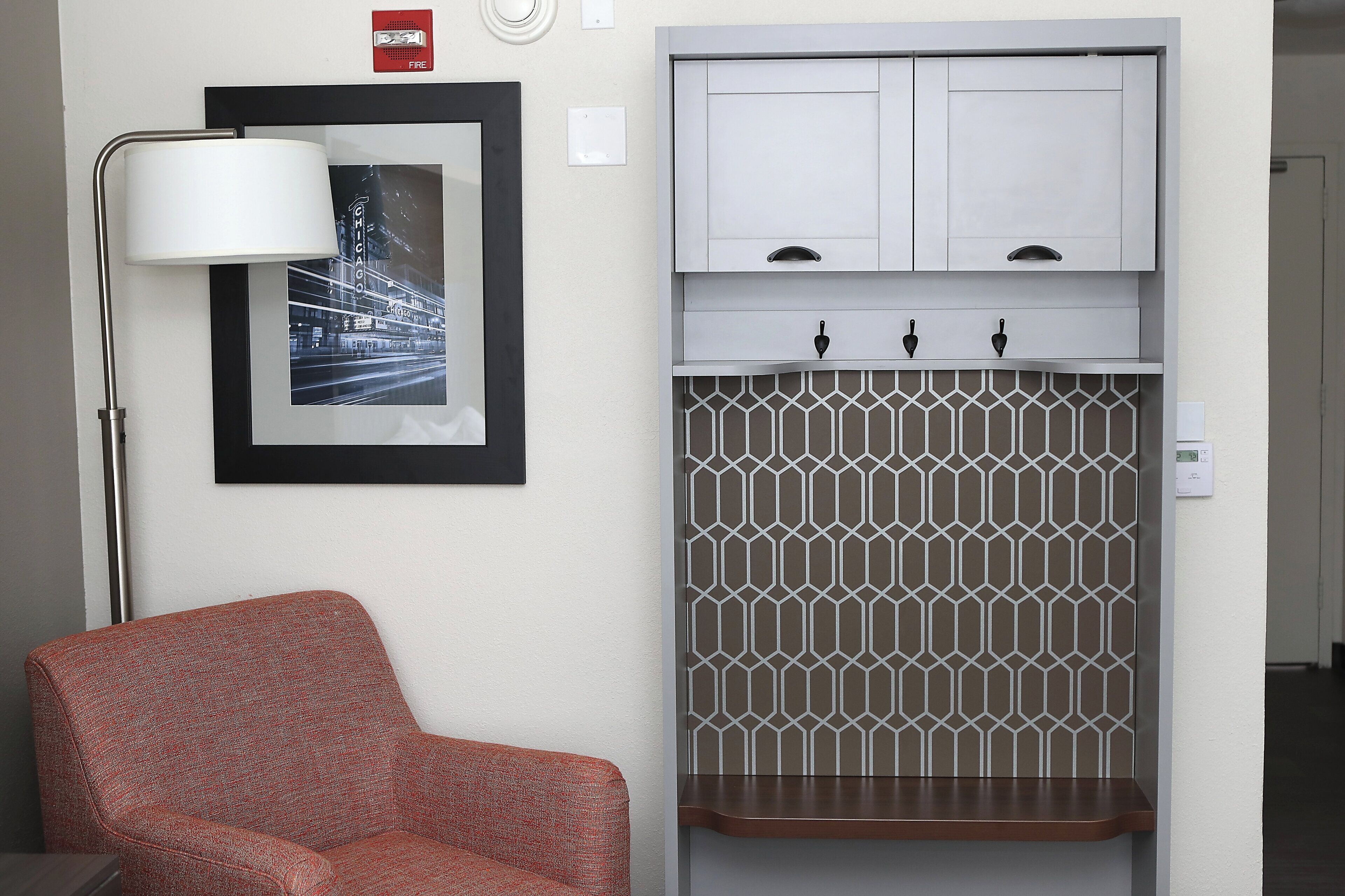A room with a red patterned sofa, a framed picture, a white cabinet, and a patterned wall.