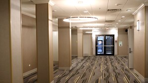 A hotel corridor with patterned carpet, beige walls, and a circular light fixture on the ceiling.