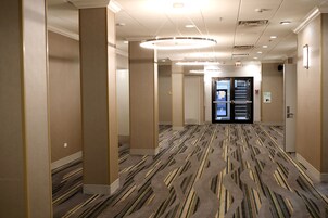 A hotel corridor with patterned carpet, beige walls, and a circular light fixture on the ceiling.