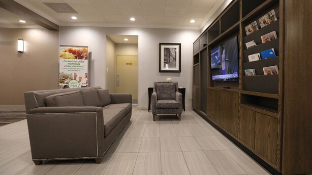 A lobby with a sofa, armchairs, a TV, magazines, and a poster.