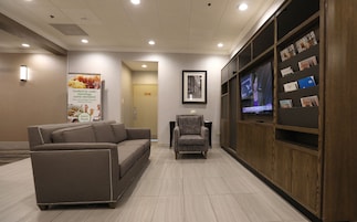 Un hall con sofá, sillones, televisor, revistas y un cartel.