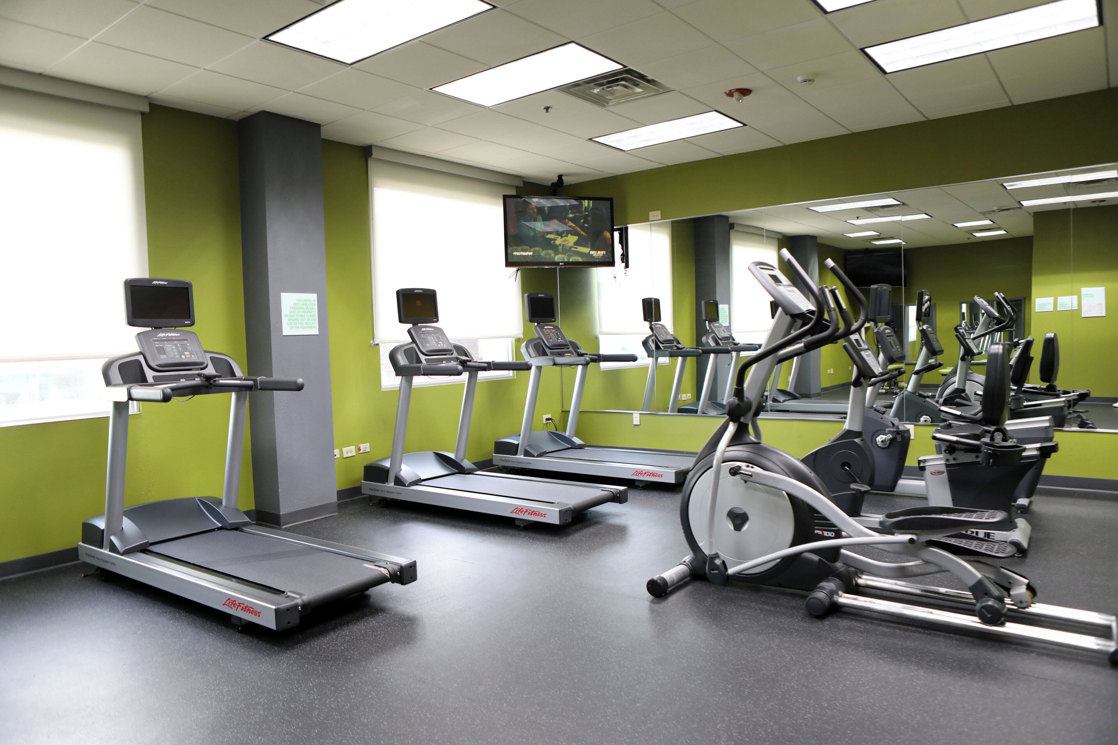 A fitness center with treadmills, elliptical machines, and a TV screen.