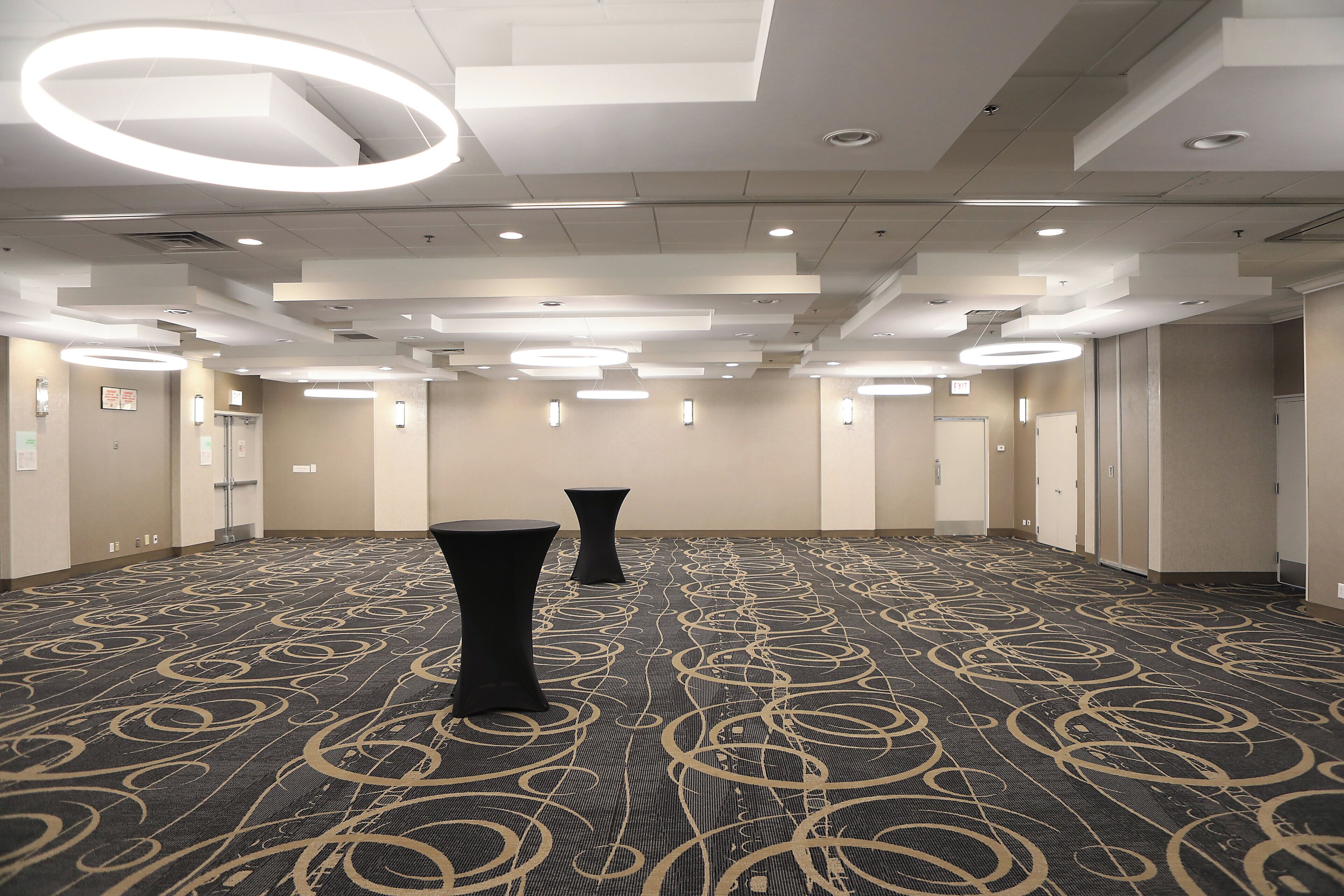 A hotel conference room with a patterned carpet, circular ceiling lights, and a 'EXIT' sign.
