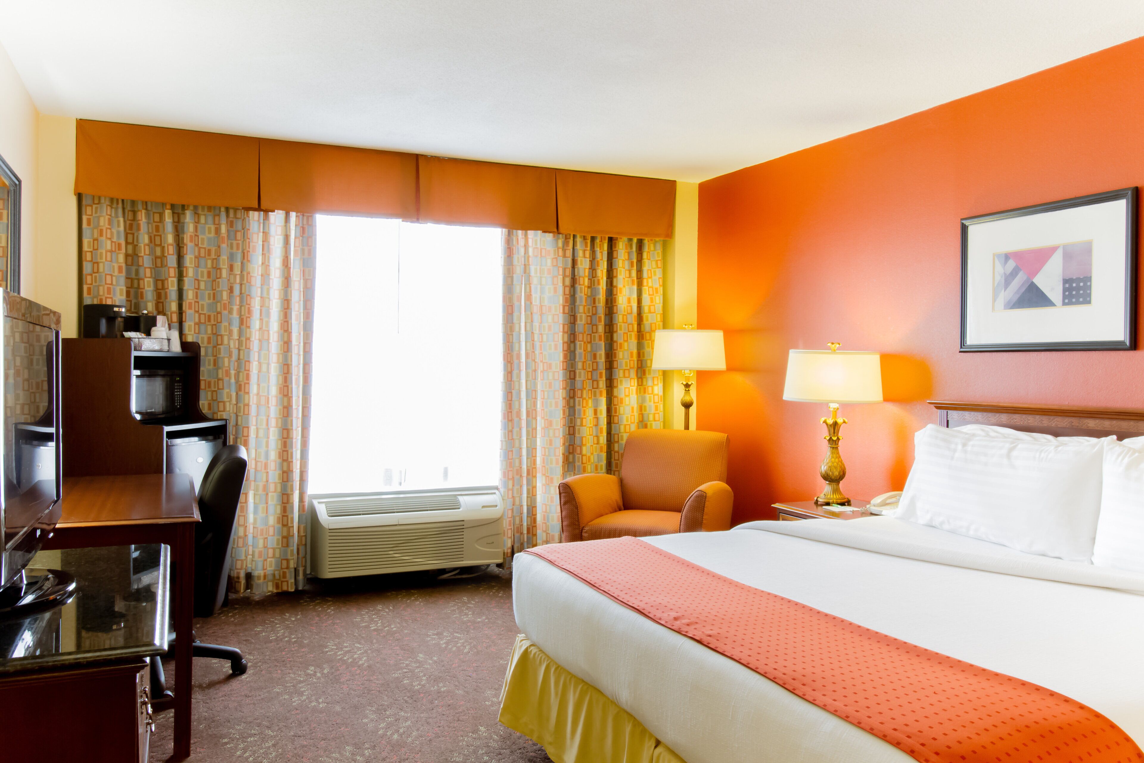 Une chambre d’hôtel équipée d’un lit, d’un bureau, d’une chaise, d’un climatiseur et d’une fenêtre avec des rideaux.