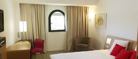 A hotel room with a bed, a desk, a chair, a TV, and a window with curtains.
