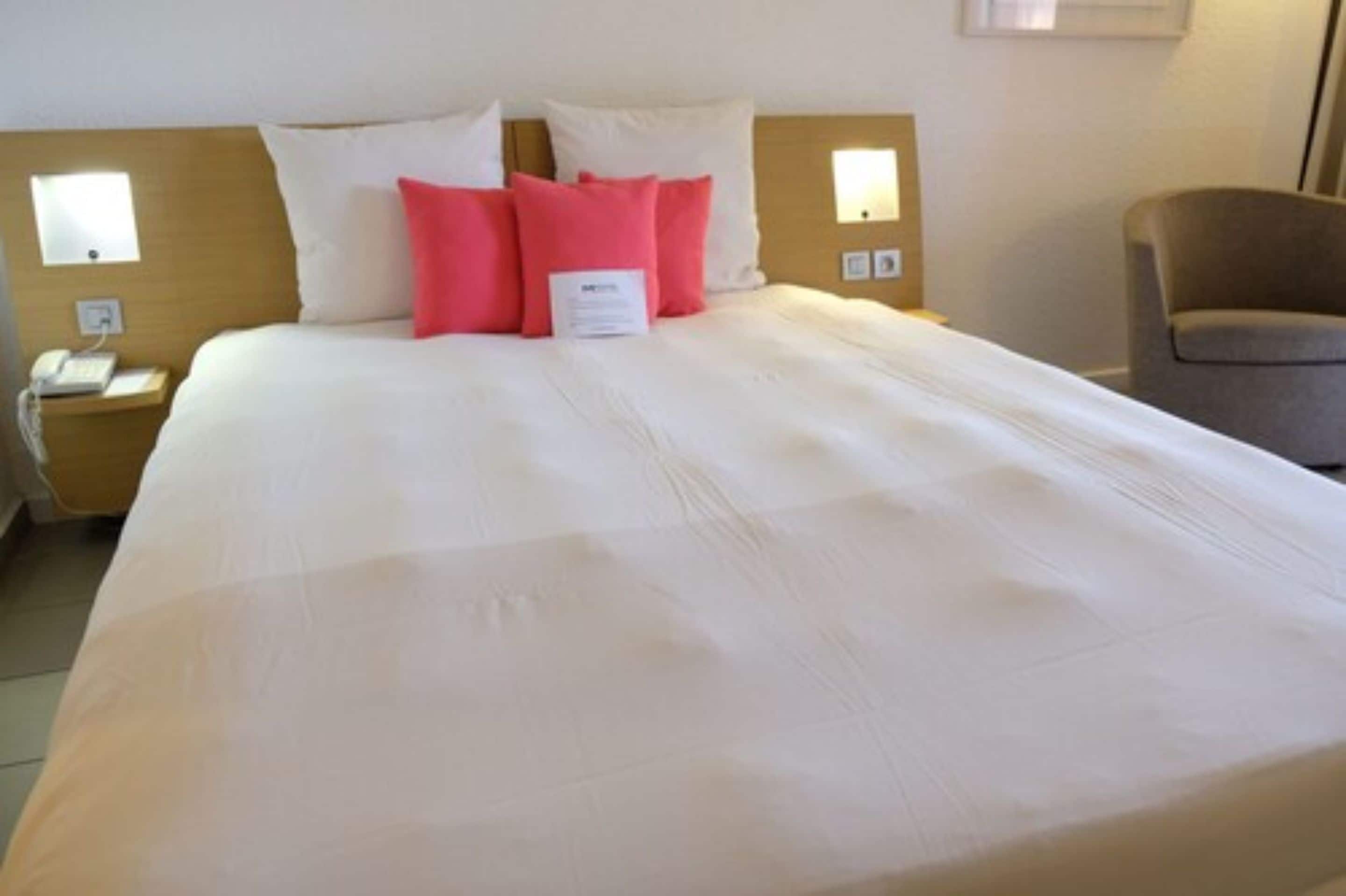 A hotel room with a large bed, two bedside tables, a chair, and a wall-mounted phone.
