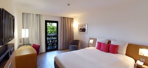 Een hotelkamer met een bed, een bureau, een stoel, een televisie en een balkon met uitzicht.