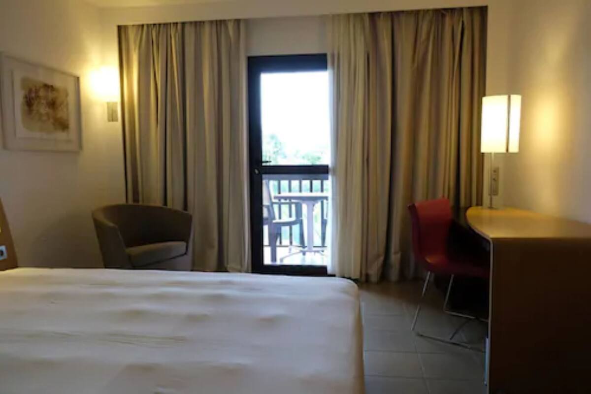 Une chambre d’hôtel avec un lit, un bureau, une chaise et un balcon.