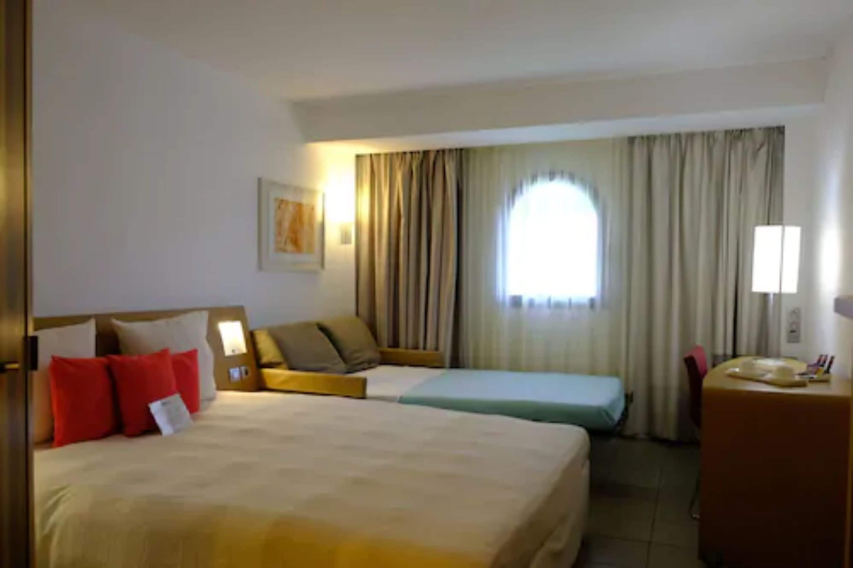Una camera d'albergo con due letti, una scrivania e una finestra con tende.