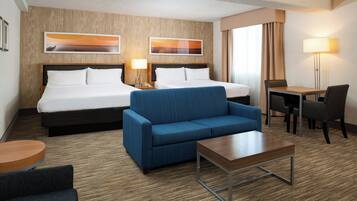 A hotel room with a double bed, a blue sofa, a small table, a desk, and a chair.