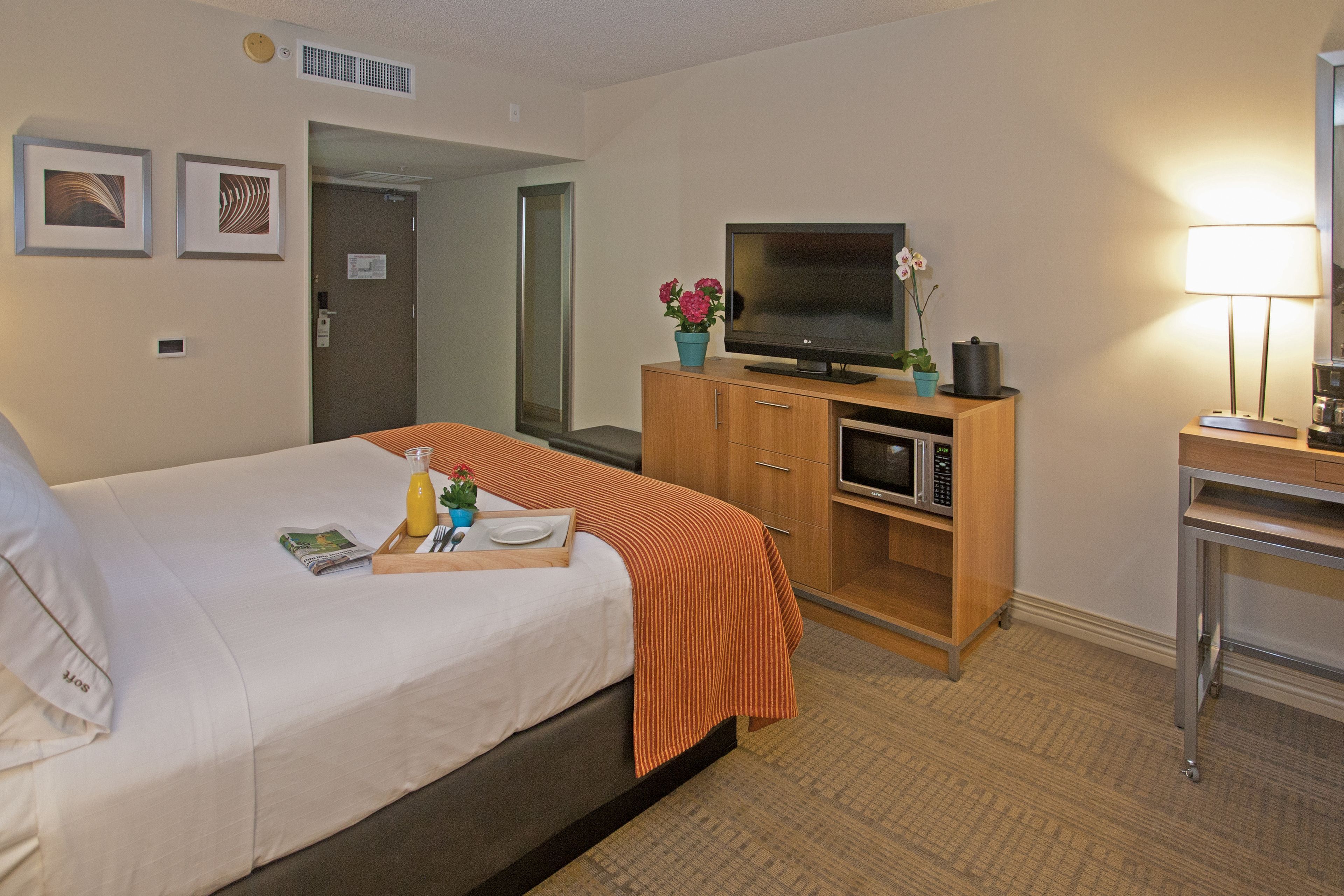 A hotel room with a bed, a television, a microwave, a desk, and a lamp.
