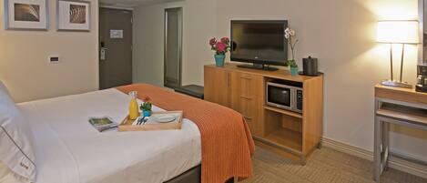 A hotel room with a bed, a television, a microwave, a desk, and a lamp.