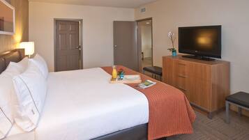 A hotel room with a bed, a television on a wooden cabinet, a desk with a chair, and a door leading to another room.
