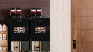 En modern kaffestation med två espressomaskiner, en trädisk och en vägg med ett geometriskt mönster.