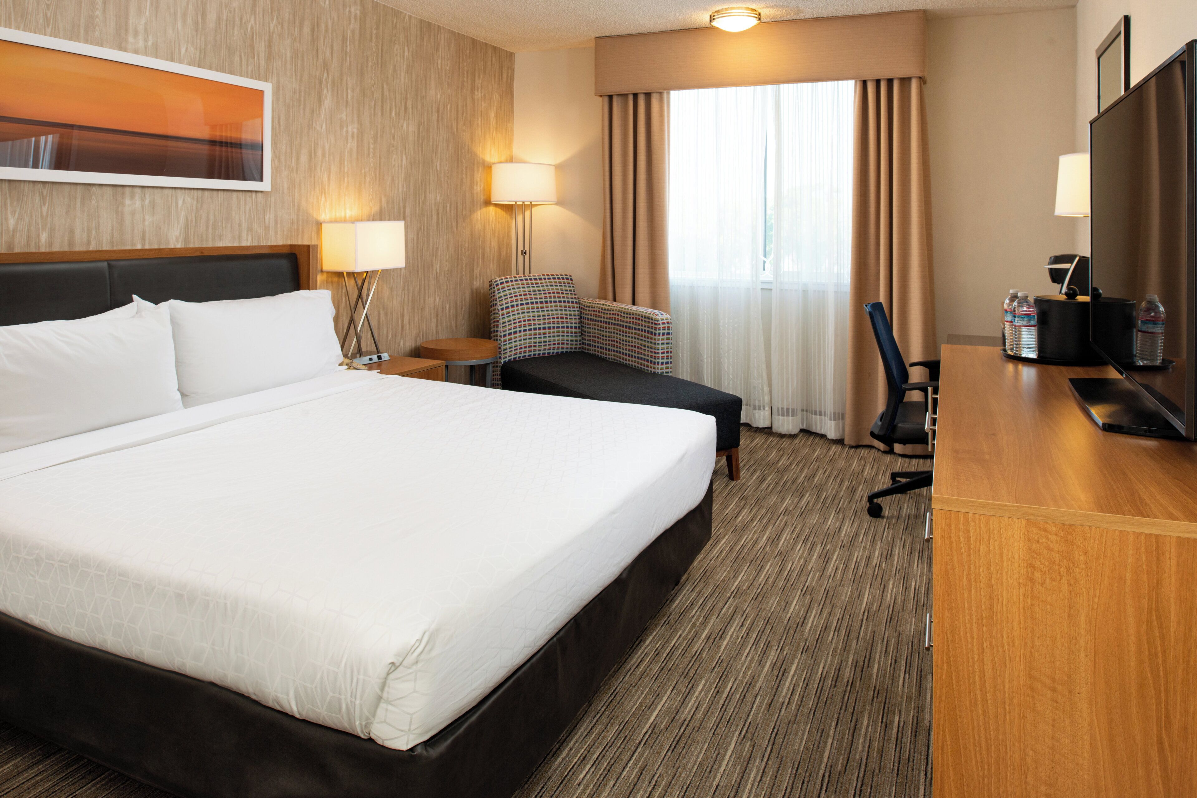 Una habitación de hotel con una cama grande, un escritorio con una silla, una lámpara y un televisor.