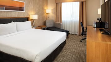 Una habitación de hotel con una cama grande, un escritorio con una silla, una lámpara y un televisor.