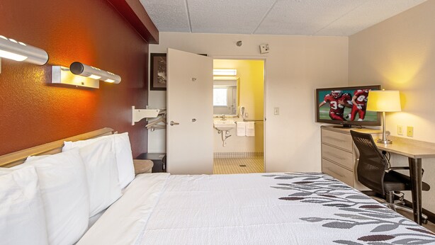 A hotel room with a bed, a desk, a chair, a television, and a bathroom visible through an open door. - Red Roof Inn Florence - Civic Center (Florence)