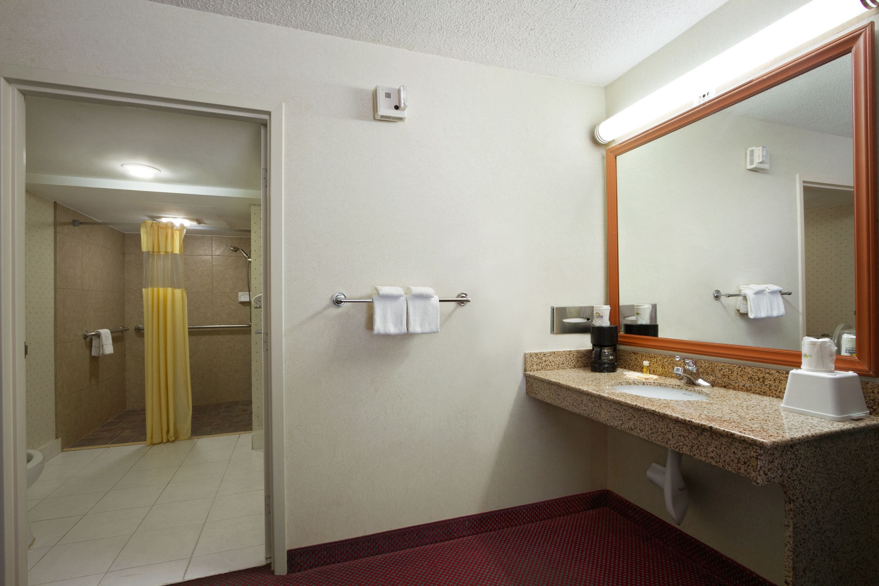A hotel bathroom with a shower, toilet, sink, and mirror.