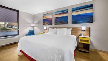 Habitación de hotel con una cama grande, una mesita de noche, una lámpara y tres cuadros de paisajes en la pared.
