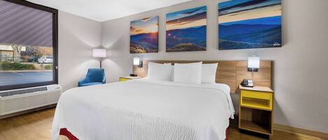 A hotel room with a large bed, a nightstand, a lamp, and three landscape paintings on the wall.