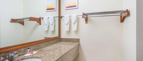 Une salle de bain avec un lavabo doté d’un plan de travail en granit, un miroir, des porte-serviettes et deux tableaux encadrés accrochés au mur.