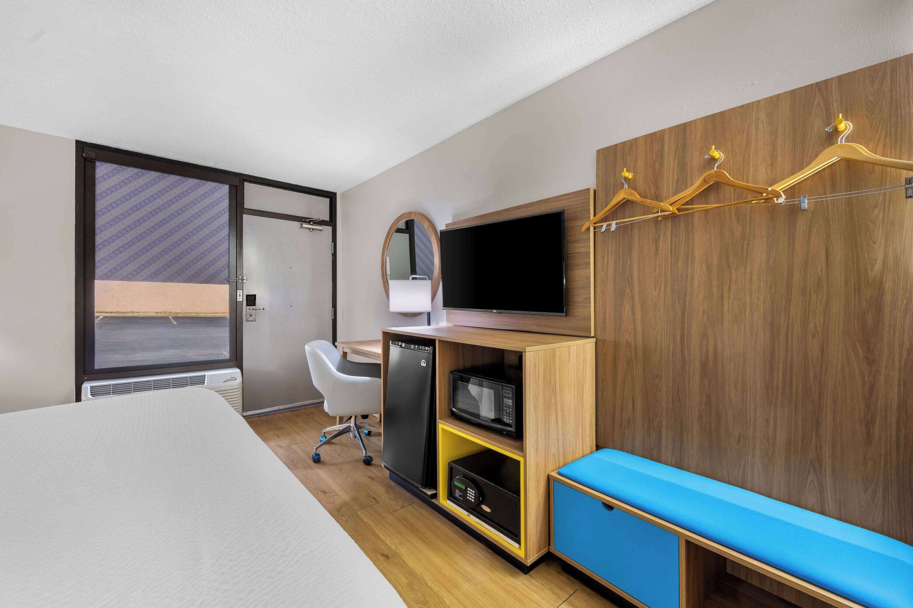 Una habitación de hotel con cama, escritorio con computadora, microondas y televisor.