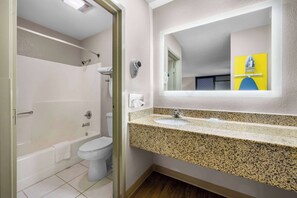 A bathroom with a white toilet, a bathtub, a sink with a granite countertop, and a mirror with a yellow accent wall.
