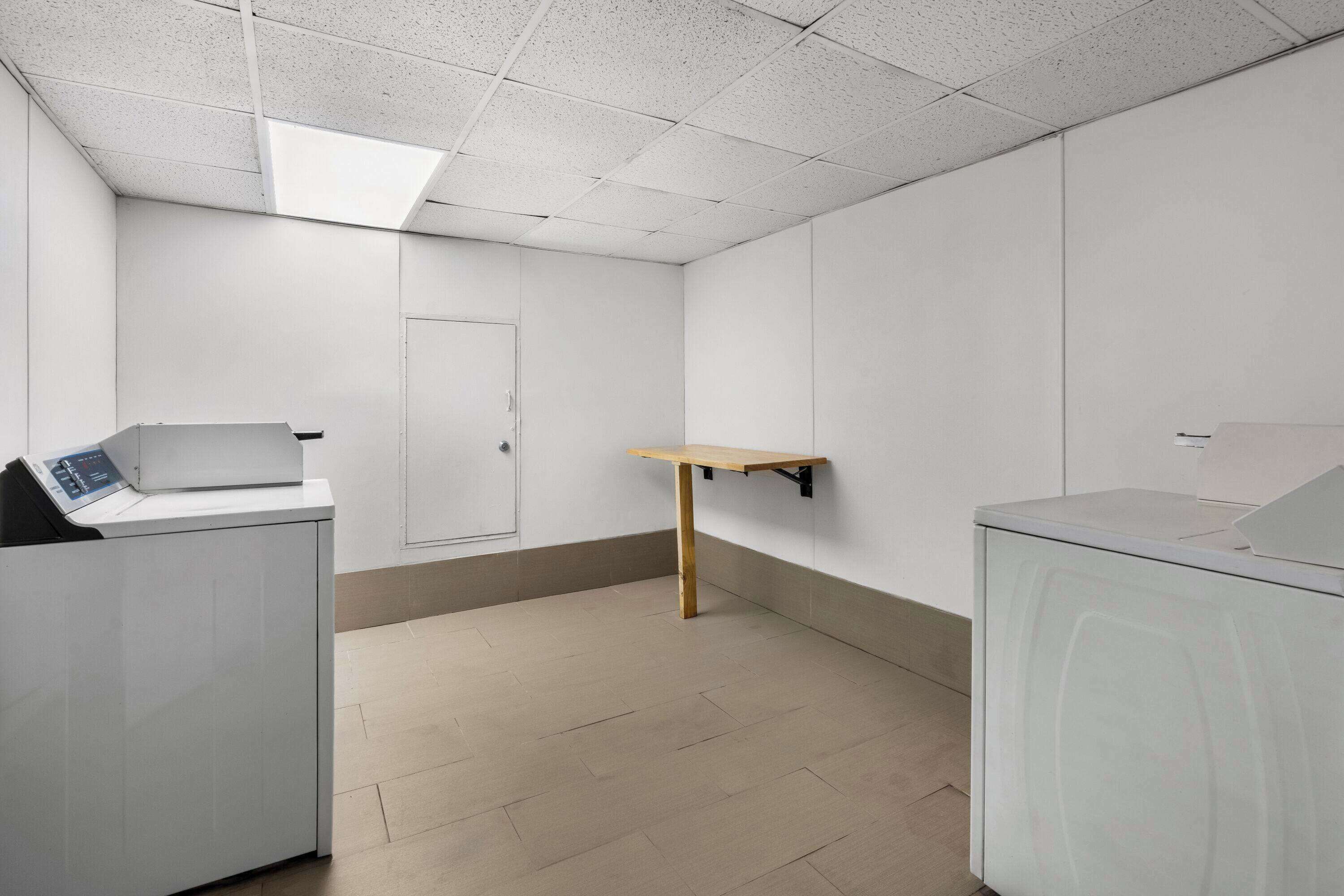 Ein Zimmer mit Waschmaschine, einem kleinen Holztisch und einer Tür.