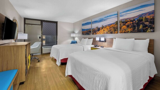 A hotel room with two beds, a desk, a chair, a TV, and artwork on the wall. - Days Inn by Wyndham Raleigh Midtown (Raleigh)