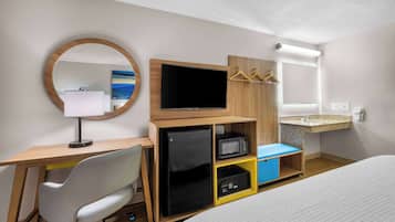 Une chambre d’hôtel équipée d’un lit, d’un bureau avec un ordinateur, d’une télévision, d’un miroir, d’un petit réfrigérateur, d’un four à micro-ondes et d’un lavabo.