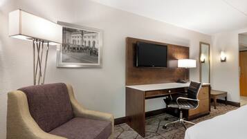 A hotel room with a bed, a desk with a chair, a television, a lamp, and a framed picture on the wall.