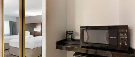 A hotel room with a bed, a small kitchenette with a microwave, and a compact refrigerator.