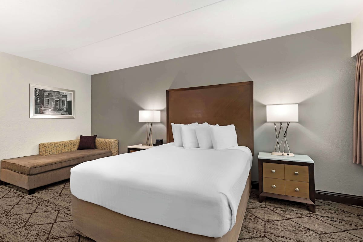 A hotel room with a large bed, a sofa, two bedside tables with lamps, and a framed picture on the wall.