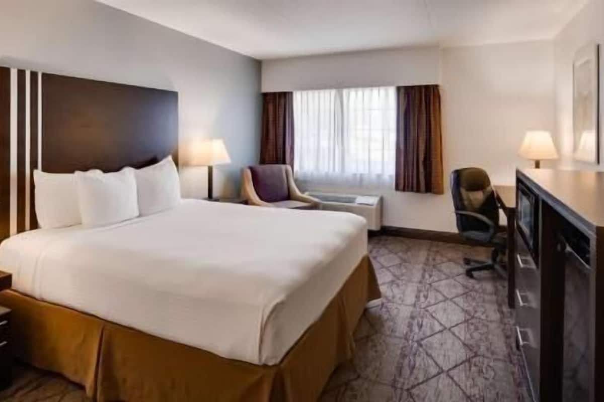 A hotel room with a large bed, a desk, a chair, a television, and a window with curtains.