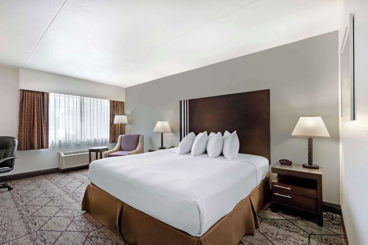 A hotel room with a large bed, two bedside tables with lamps, a chair, a desk, and a window with curtains.